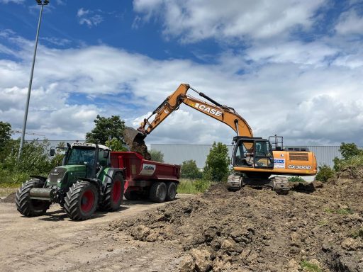 Baumaschinen auf einer Baustelle, ein Traktor und ein Bagger bearbeiten den Boden.