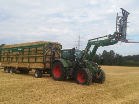 Traktor mit Ballengabel beim Transport von Strohballen auf einem Feld in Nordrhein-Westfalen