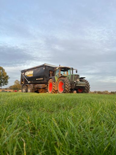 Schwarzer Traktor mit Anhänger auf grünem Feld unter bewölktem Himmel.